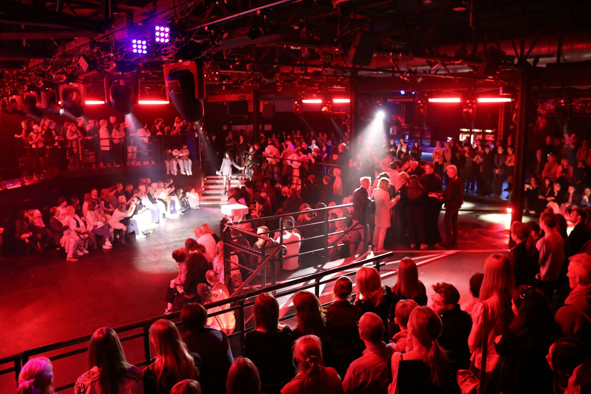 Viele Menschen sind in einem riesigen rot beleuchteten mehrstöckigen Discoraum versammelt.