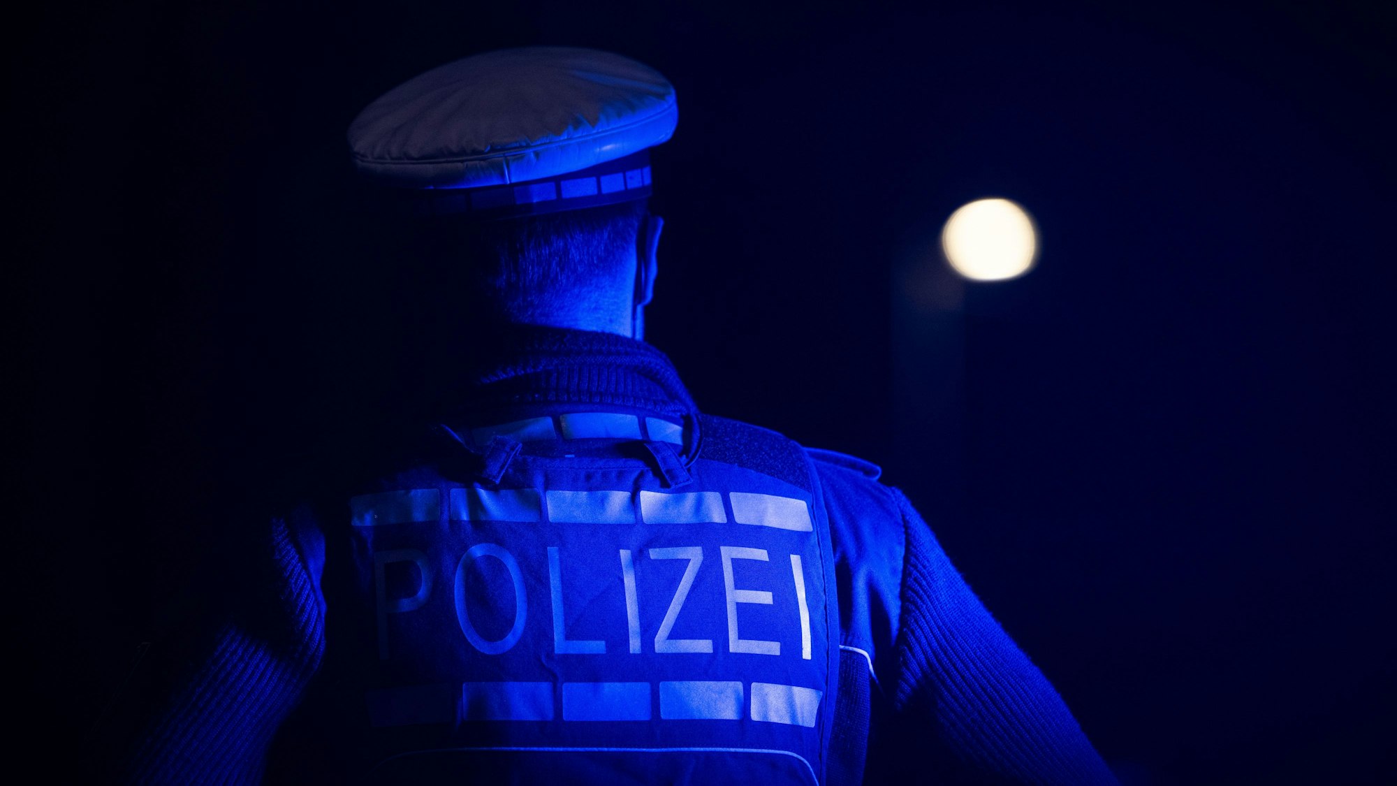 Ein Polizist steht neben einem Polizeifahrzeug (gestellte Szene).