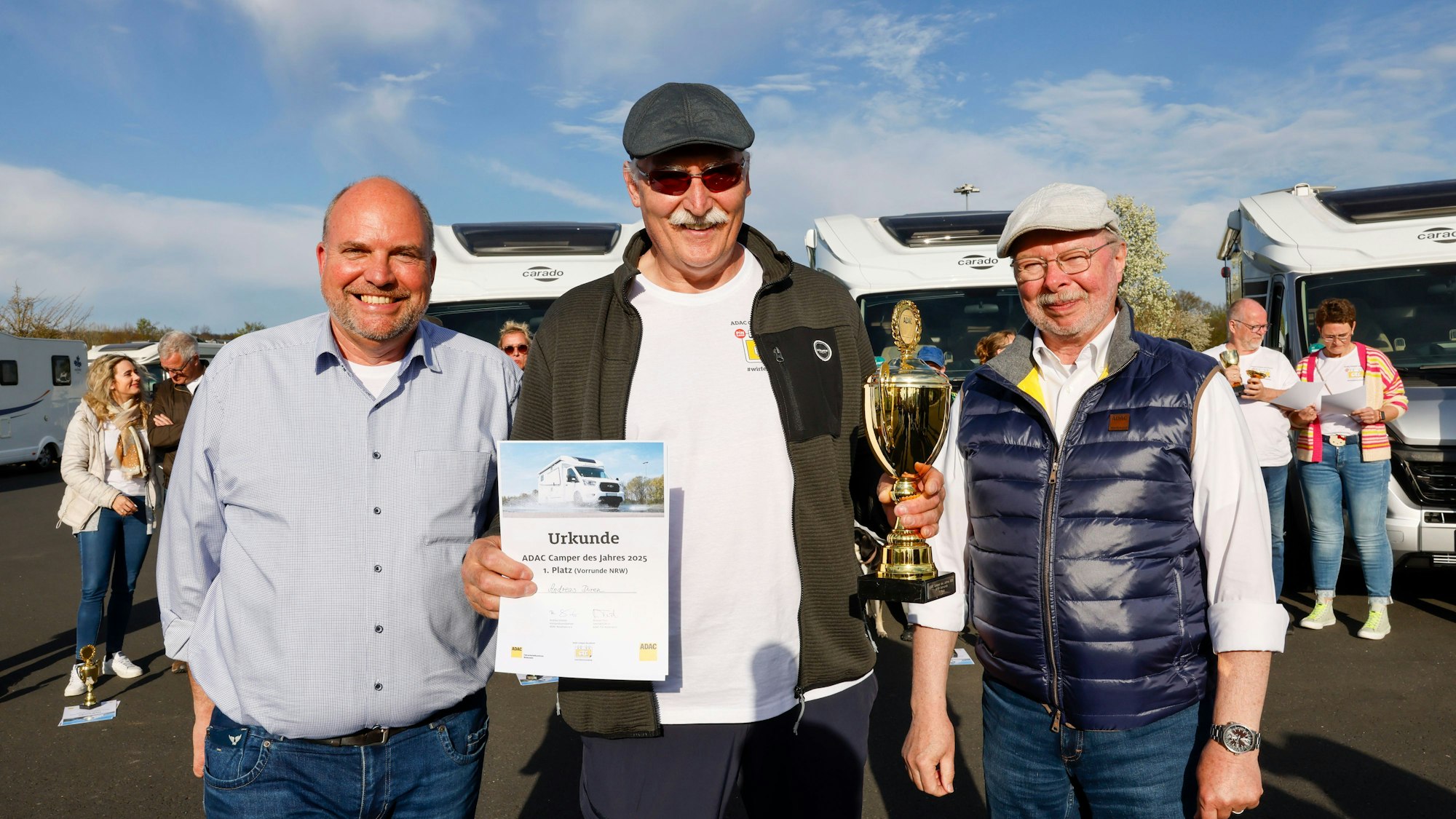 Andreas Düren hält eine Urkunde und einen Pokal in der Hand. Michael Tück, Leiter des ADAC Fahrsicherheitszentrums Rhein-Erft, und Bernd Birkholz, ADAC Nordrhein, haben ihn in ihre Mitte genommen.