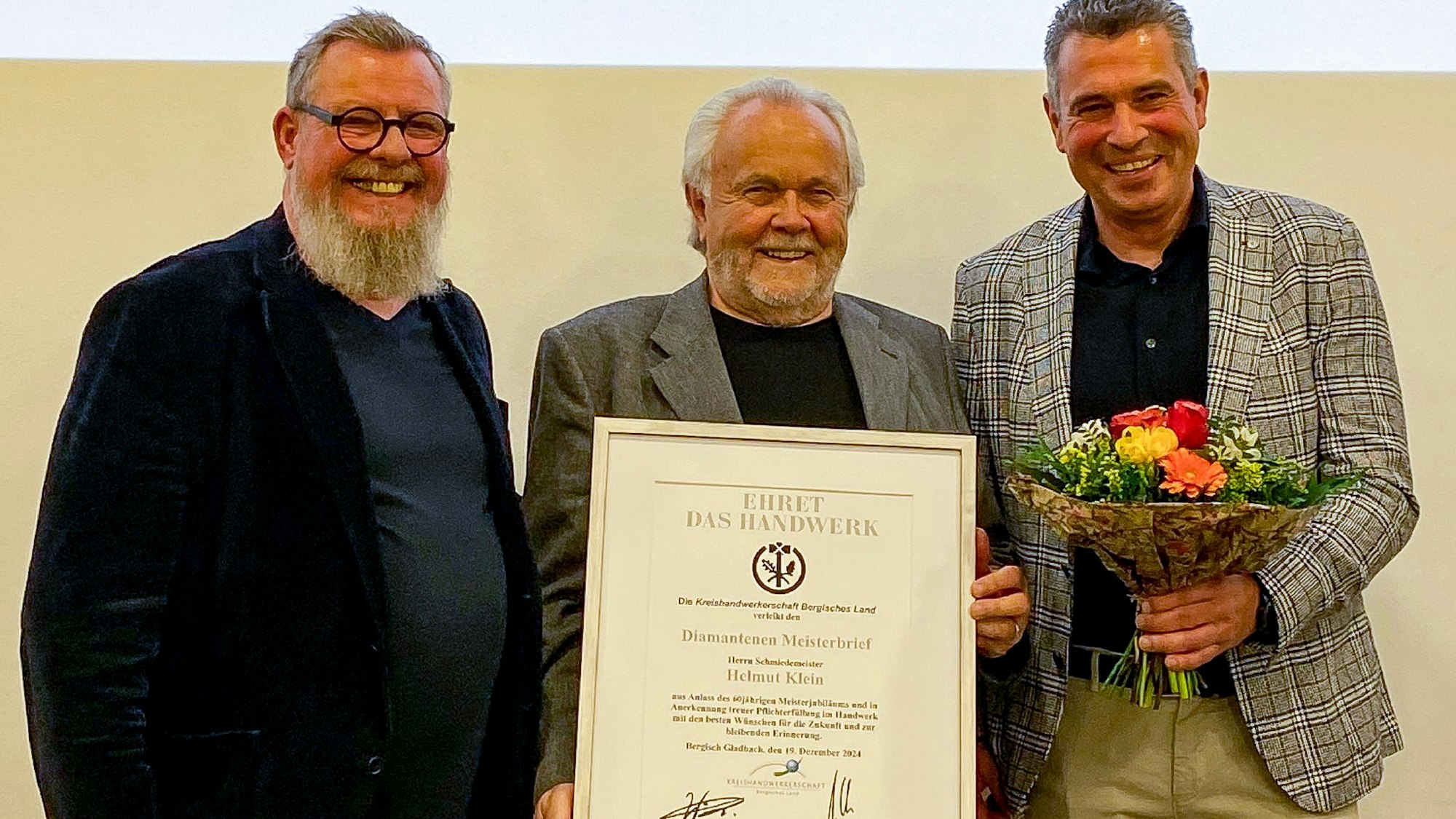 Zwei Männer überreichen einen Diamantenen Meisterbrief an Helmut Klein.