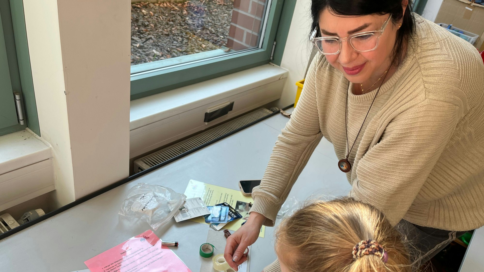 Eine Frau mit dunklem Haar und Brille zeigt einem Mädchen, wie man einen Mini-Motor baut.