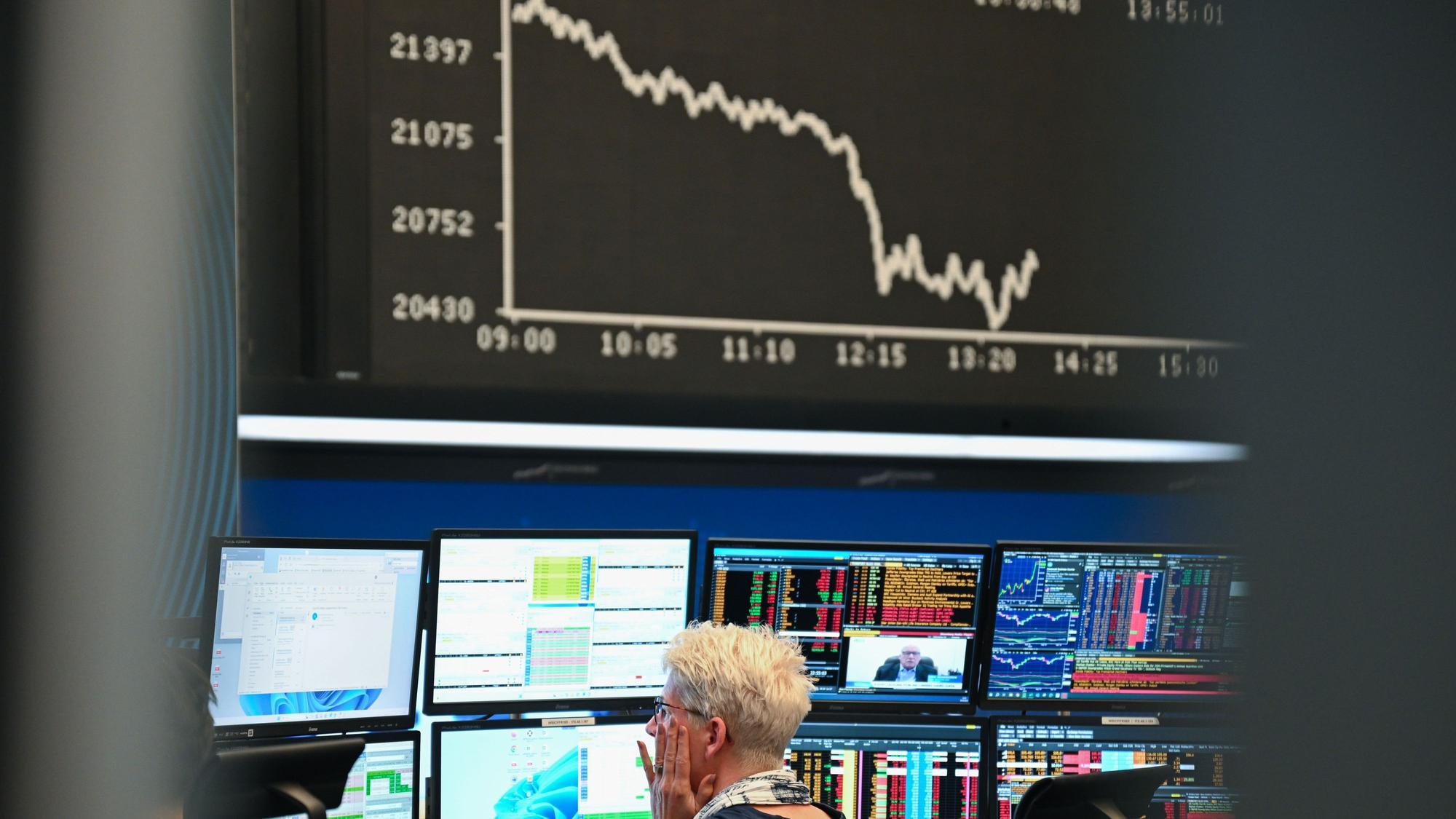 Eine Börsenhändlerin beobachtet auf dem Parkett der Frankfurter Wertpapierbörse ihre Monitore, während die Anzeigetafel mit der Dax-Kurve fallende Kurse anzeigt. US-Präsident Donald Trump hatte ein gewaltiges Zollpaket gegen Handelspartner in aller Welt erlassen.