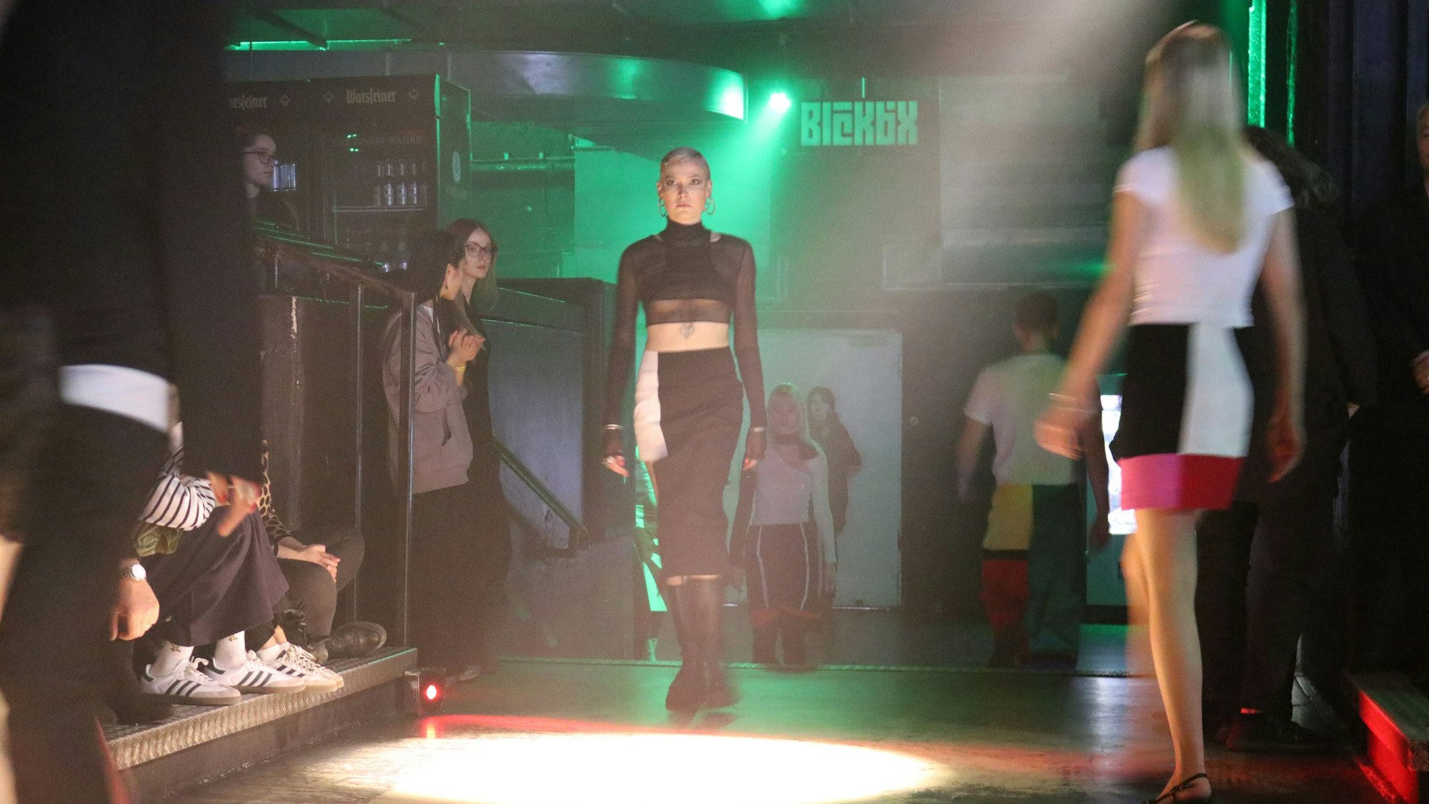 Models laufen über eine von Scheinwerfern ausgeleuchtete Tanzfläche.
