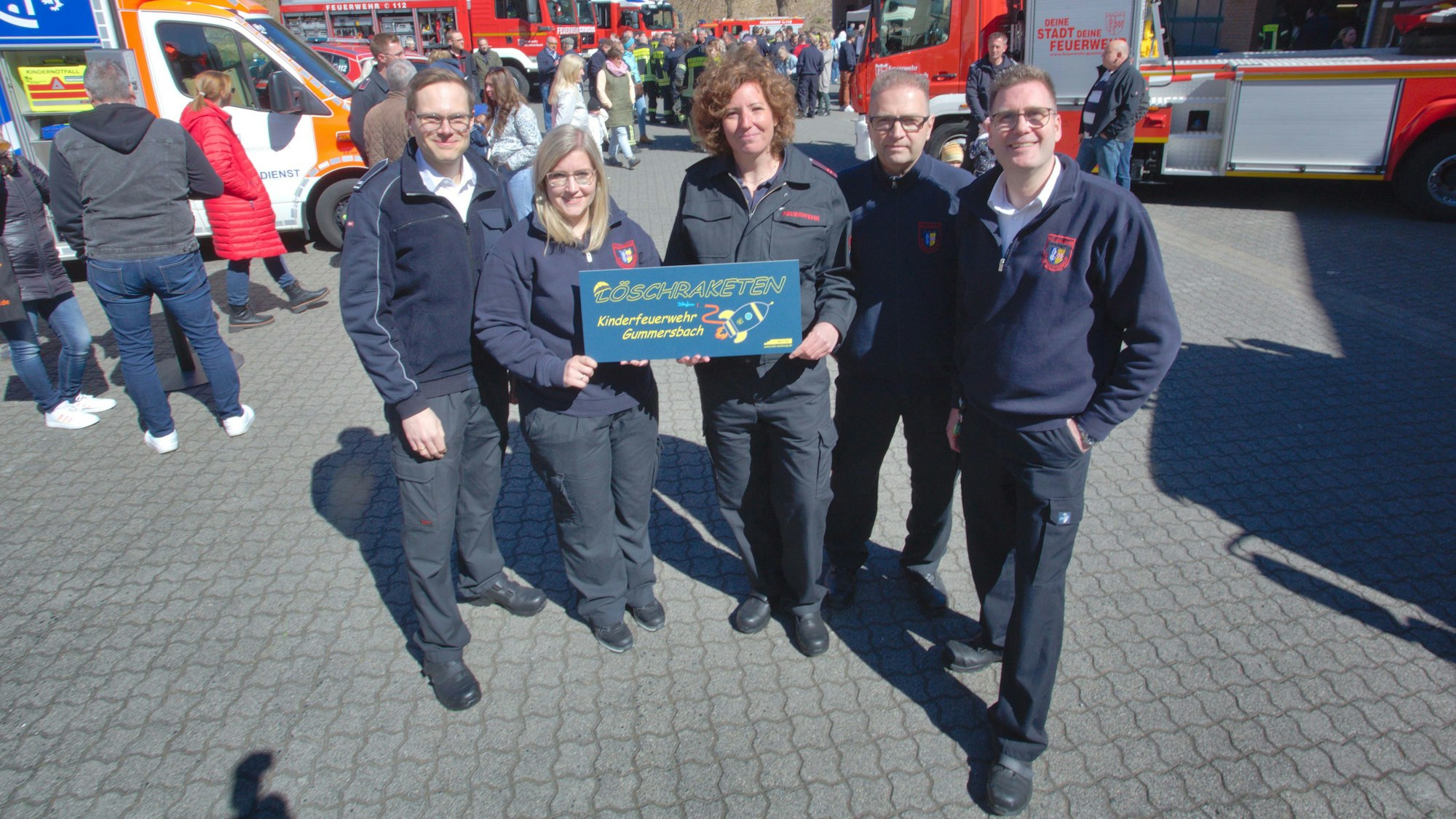 Mehrere Mitglieder der Feuerwehr halten gemeinsam ein Schild hoch, auf dem der Name der neuen Gummersbacher Kinderfeuerwehr, „Löschraketen“, steht.