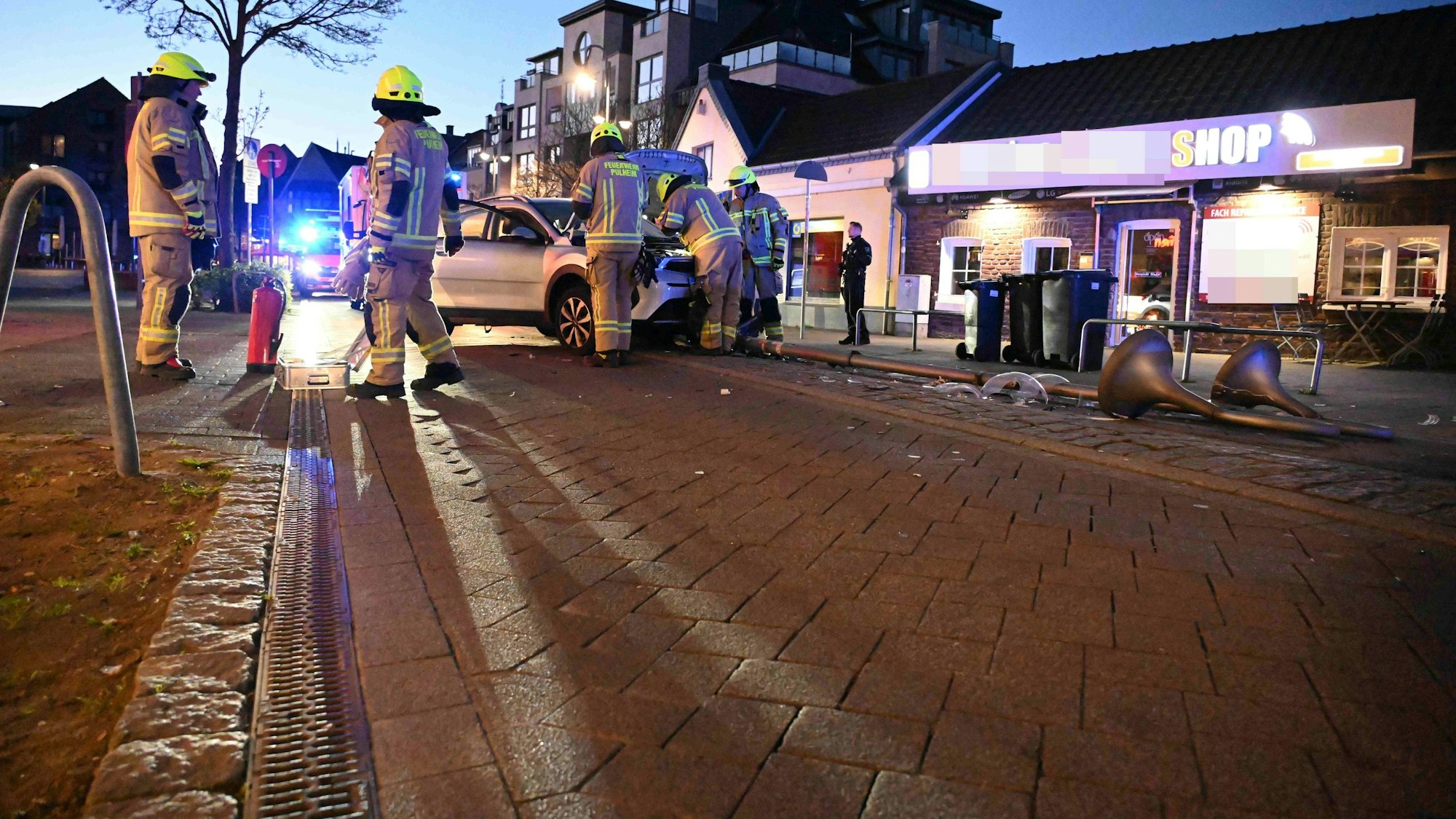 Feuerwehrleute stehen in der Nähe eines Pkw, der mit einer Straßenlaterne kollidiert war.