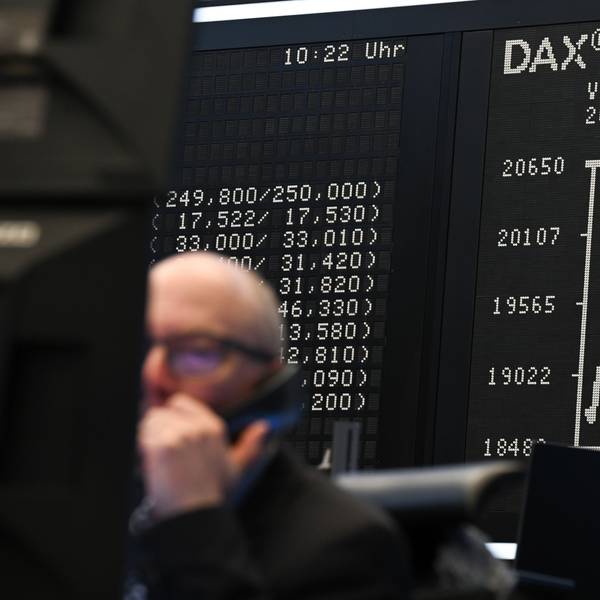 Während ein Börsenhändler auf dem Parkett der Frankfurter Börse vor seinen Monitoren sitzt, zeigt die Anzeigetafel mit der Dax-Kurve einen Wert von unter 20.000 Punkten an.