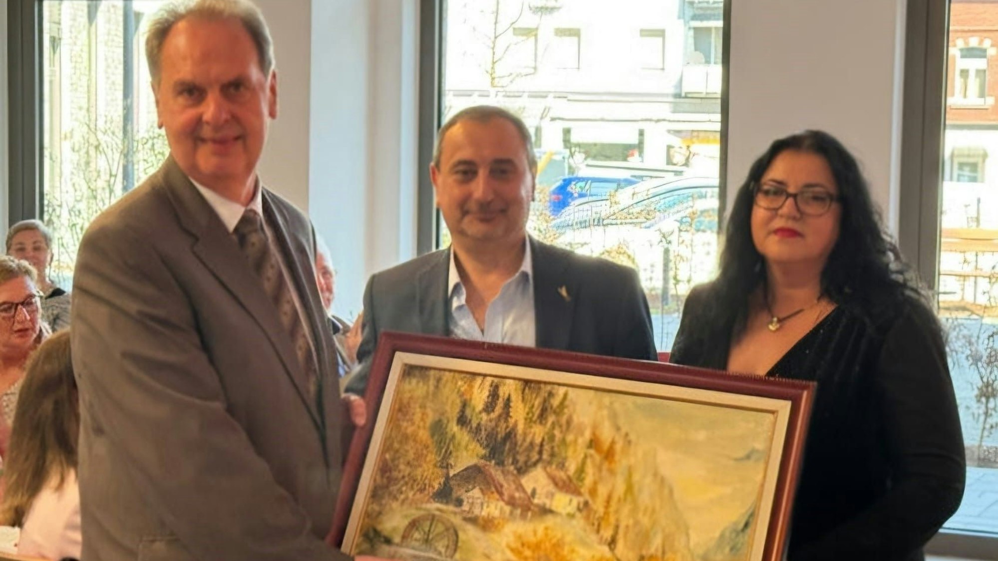 Ein Mann und eine Frau überreichen einem weiteren Mann ein handgemaltes Gemälde.