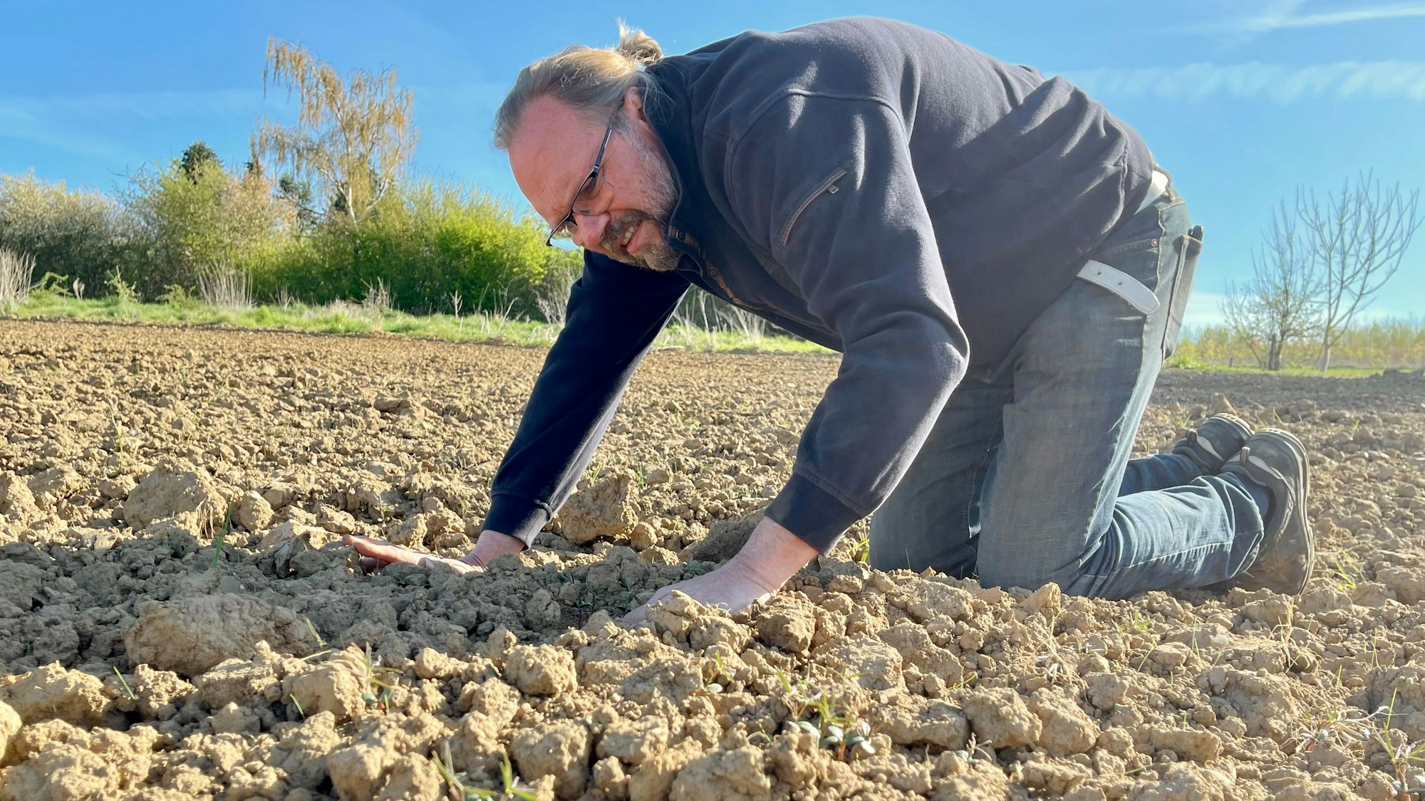 Bernd Dornbusch kniet auf seinem trockenen Feld, die Hände auf die krümelige, trockene Erde gelegt.