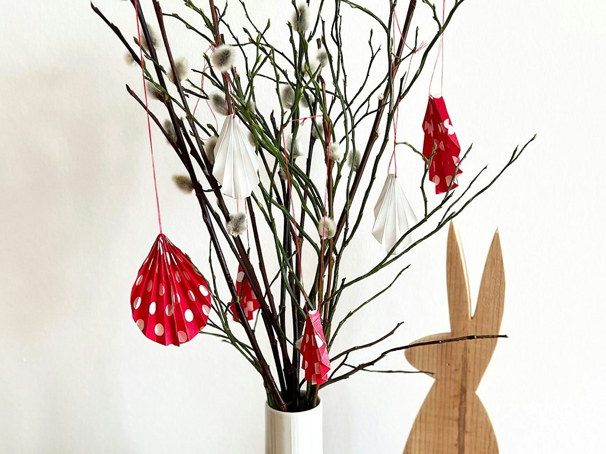 Selbstgemachter Osterschmuck: Aus buntem, gefaltetem Papier werden Anhänger für den Osterstrauß.