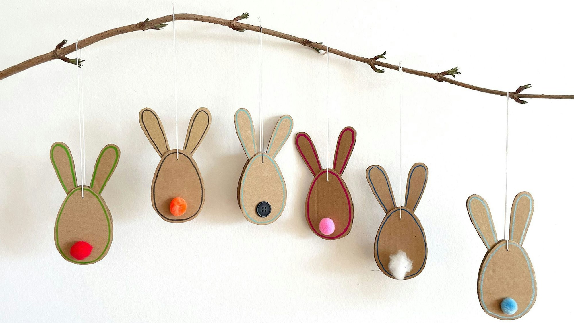 Schnelle Hasen: Aus einem unbedruckten Versandkarton und bunten Bommeln entstehen schöne Osteranhänger.
