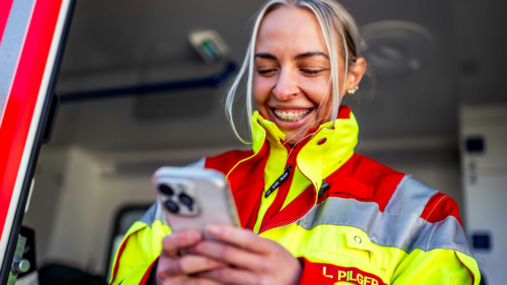 Das Bild zeigt Lea Pilger in ihrer Rettungsdienstkleidung. Sie hält ein Smartphone in der Hand hat.