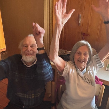 Auf dem Bild ist ein älteres Ehepaar zu sehen, das Sitz-Gymnastik macht.