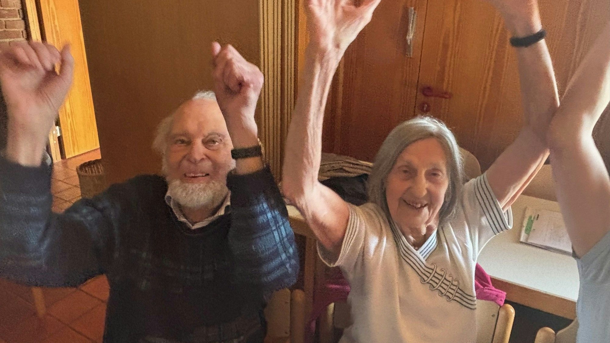 Auf dem Bild ist ein älteres Ehepaar zu sehen, das Sitz-Gymnastik macht.