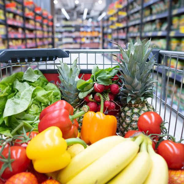 Ein Einkaufskorb mit Obst und Gemüse steht in einem Supermarkt.