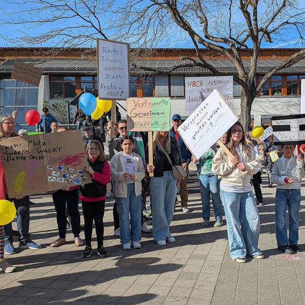 Schüler und Eltern halten auf dem Schulhof Protestplakate hoch.