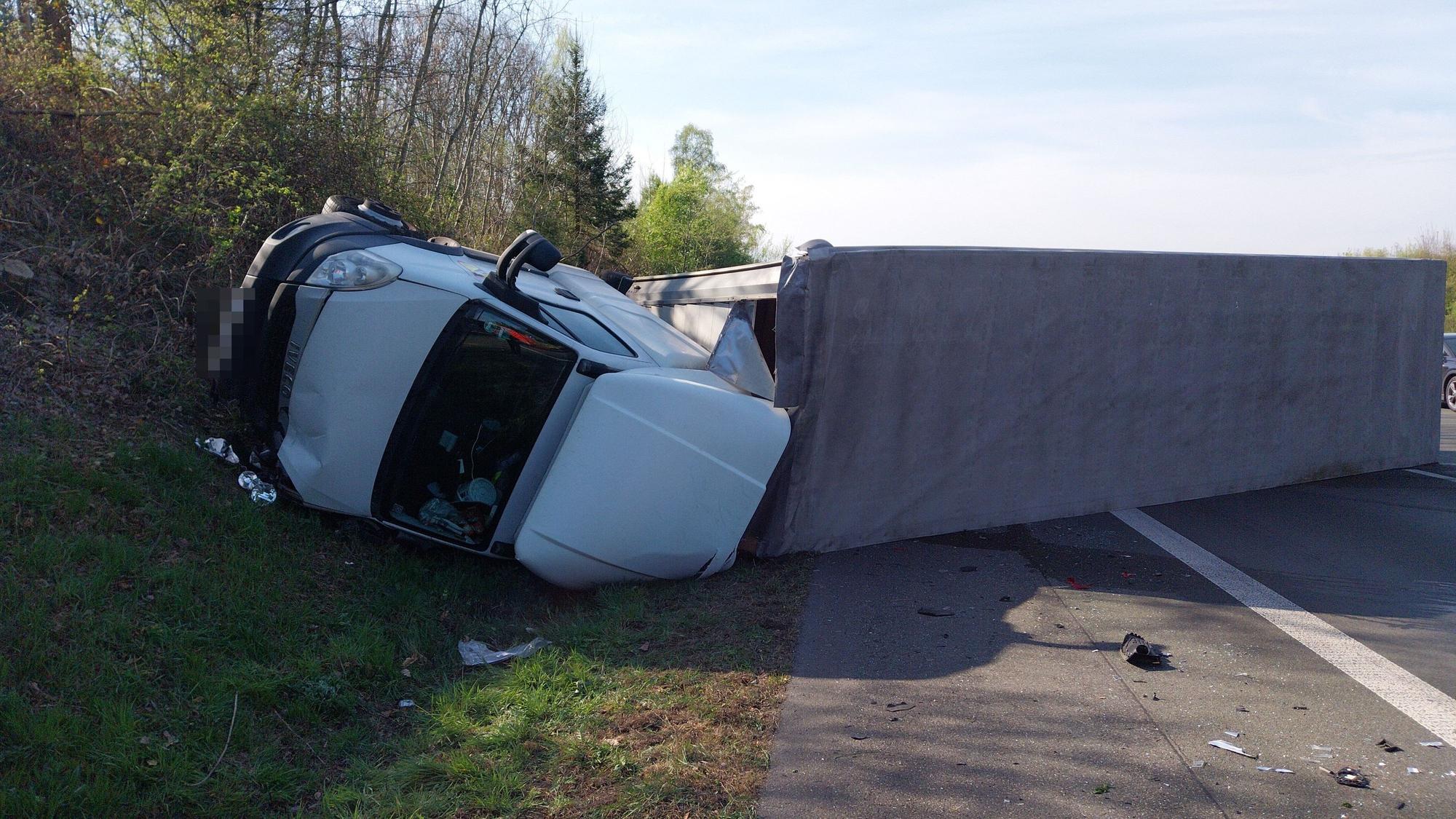 Ein Lastwagen mit Anhänger liegt umgekippt in einer Böschung..