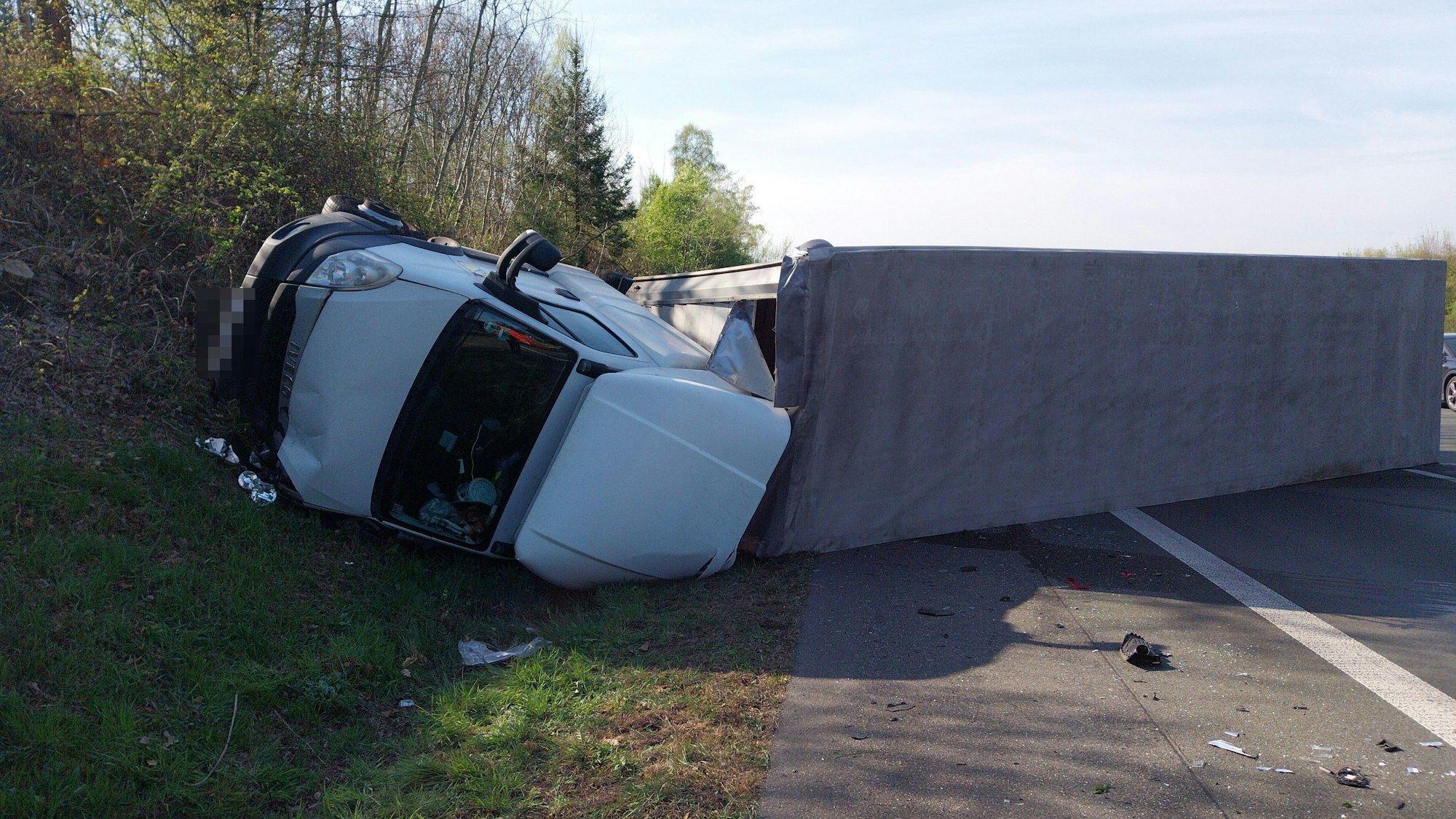 Ein Lastwagen mit Anhänger liegt umgekippt in einer Böschung..