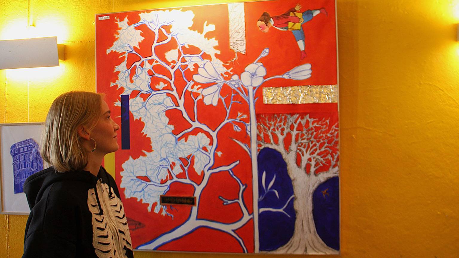Eine Frau schaut auf ein rot-buntes Bild an einer gelben Wand.