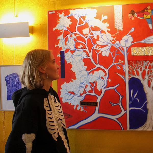 Eine Frau schaut auf ein rot-buntes Bild an einer gelben Wand.