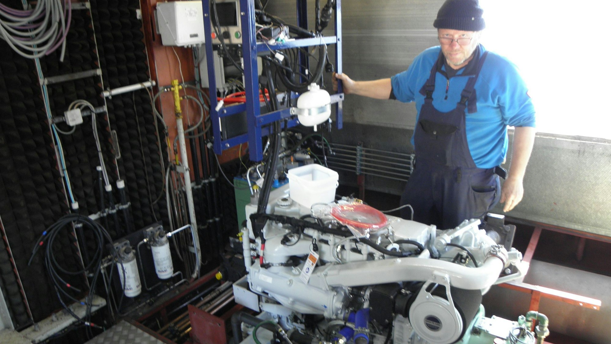 Kapitän Klaus Blumberg. steht in blauer Arbeitskleidung und mit Mütze an einem der beiden neu installierten Schiffsmotoren.