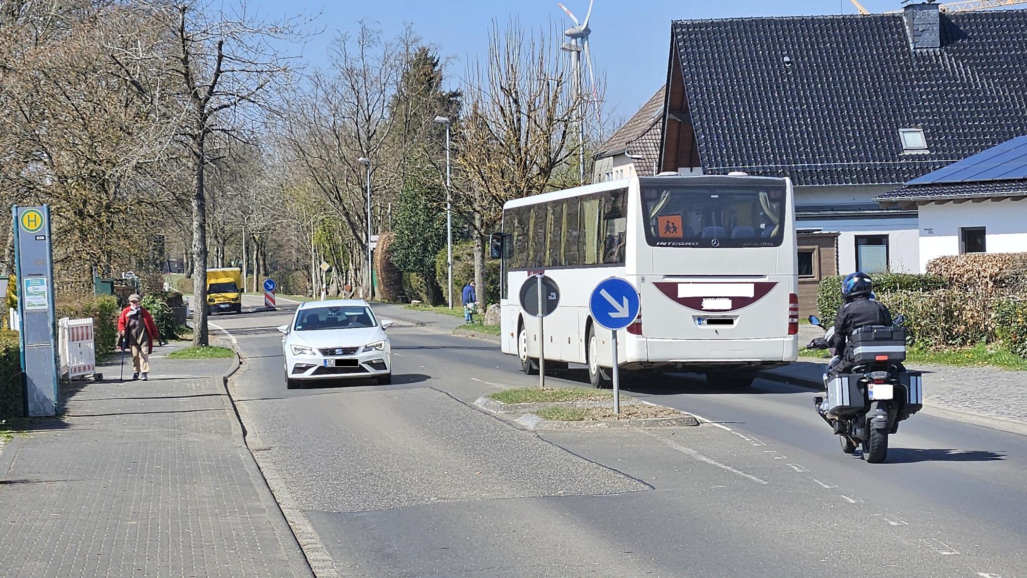 Ein Bus, ein Auto und ein Motorrad fahren an einer Querungshilfe vorbei.