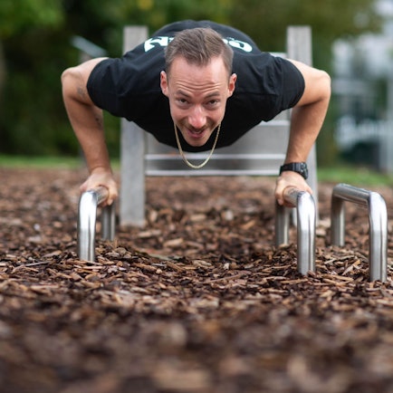 Ein Mann trainiert an einem Fitnessgerät in einem Park.