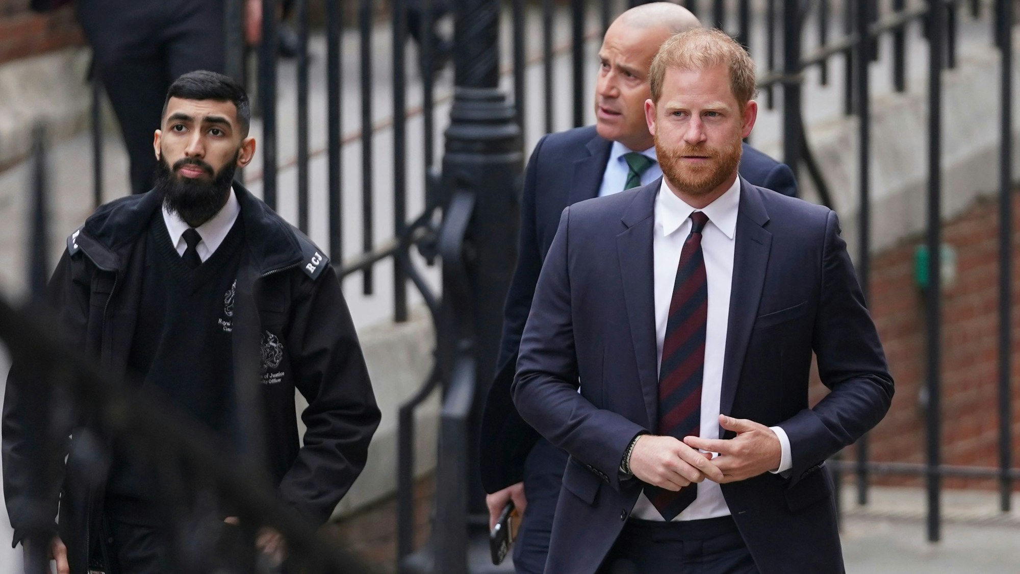 Prinz Harry (r) wird von Sicherheitskräften eskortiert, als er am Royal Courts of Justice eintrifft.