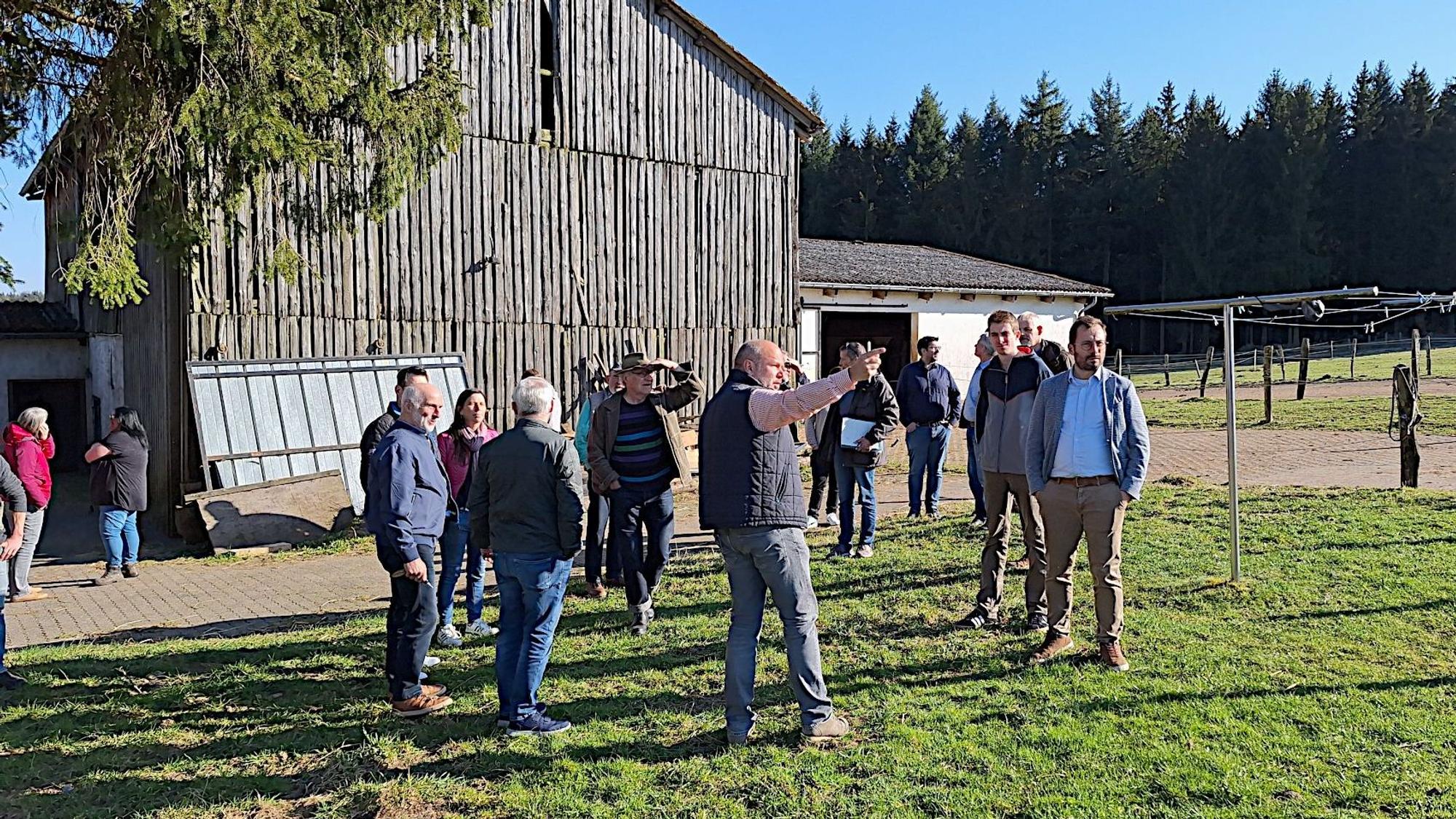 Eine Gruppe steht auf einer Wiese und schaut sich ein Gebiet an, auf dem in der Gemeinde Dahlem ein Solarpark geplant werden soll.
