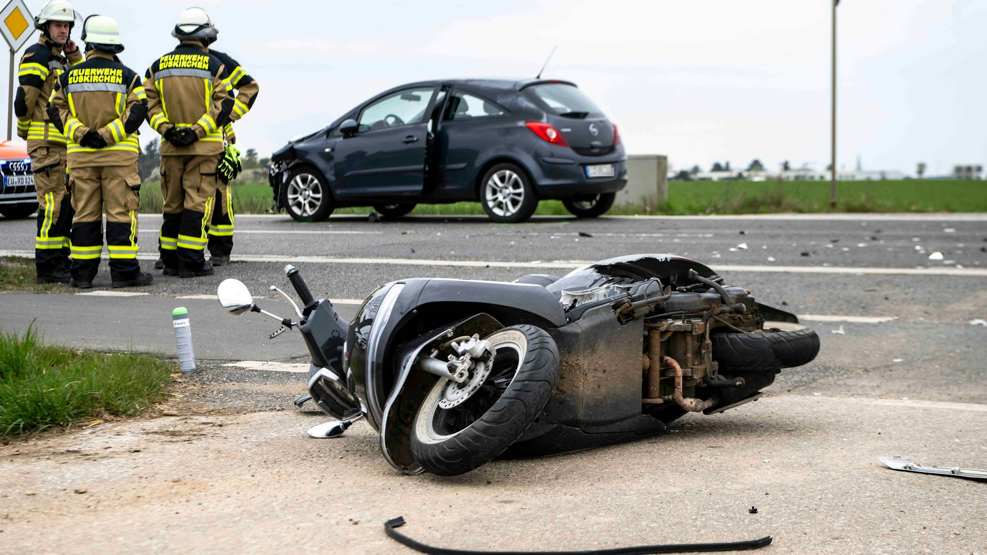 Das Bild zeigt den Roller, der auf der Seite liegt. Im Hintergrund ist ein Auto zu sehen.