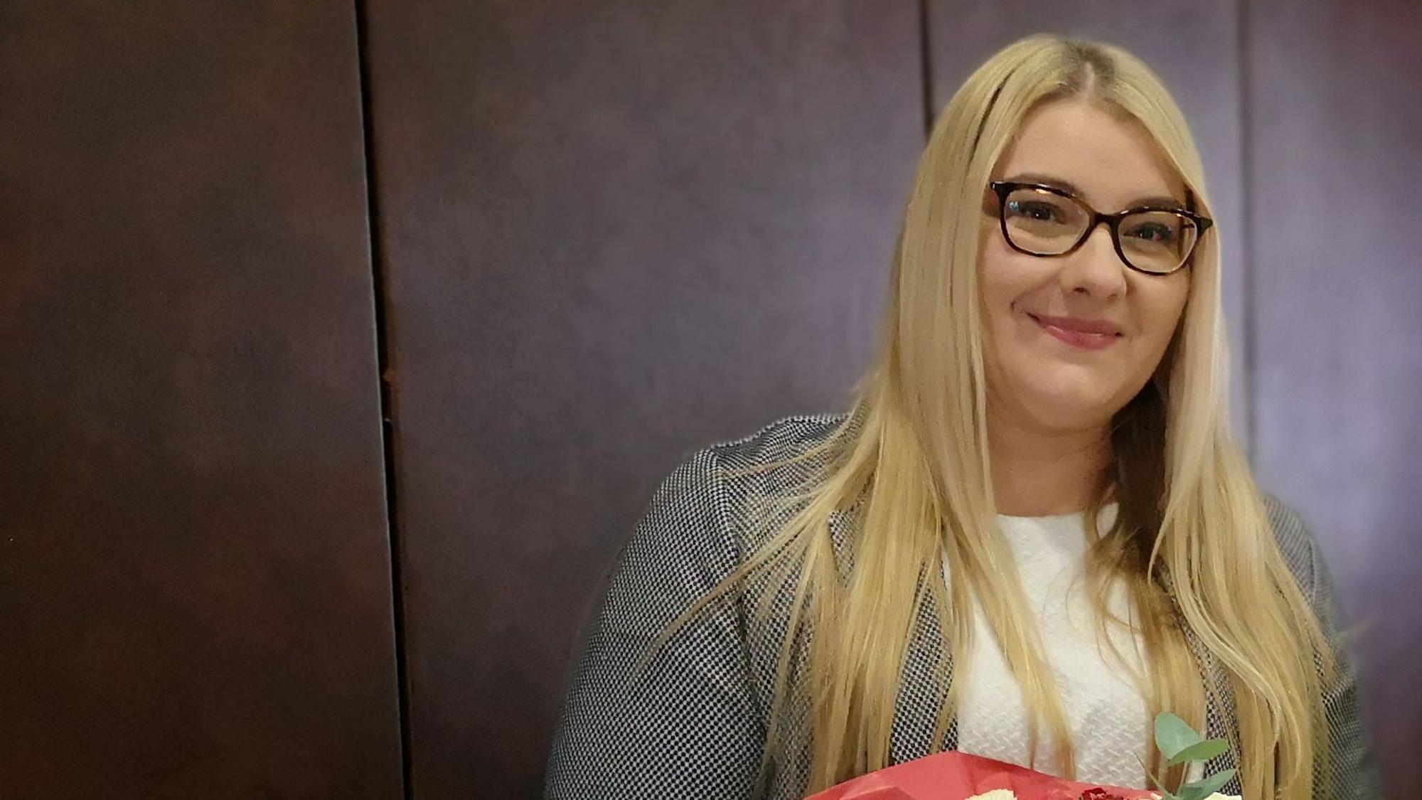 Auf dem Foto ist eine Frau mit langem blonden Haar und einer Brille zu sehen.
