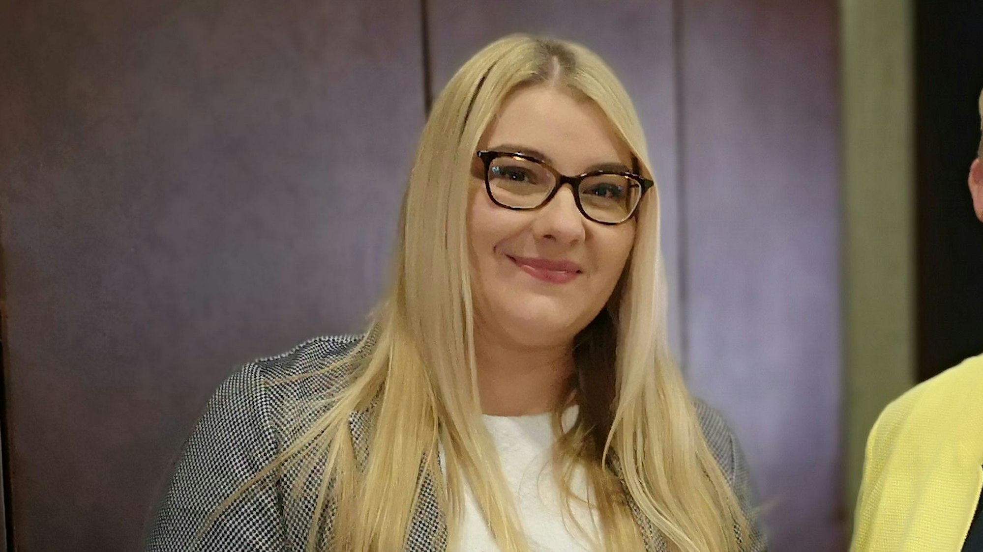 Auf dem Foto ist eine Frau mit blondem Haar und einer schwarzen Brille zu sehen.