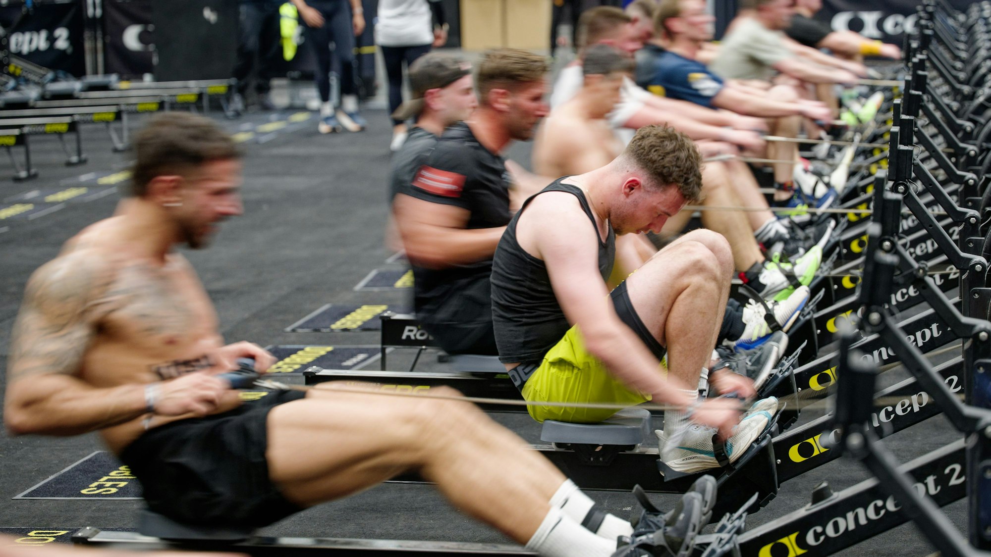 Teilnehmer rudern als Teil eines Indoor-Fitness-Wettkampfs mit Kraft-, Konditions- und Ausdauerübungen.