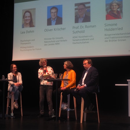 Männer und Frauen sitzen auf Hochstühlen auf einer Bühne.