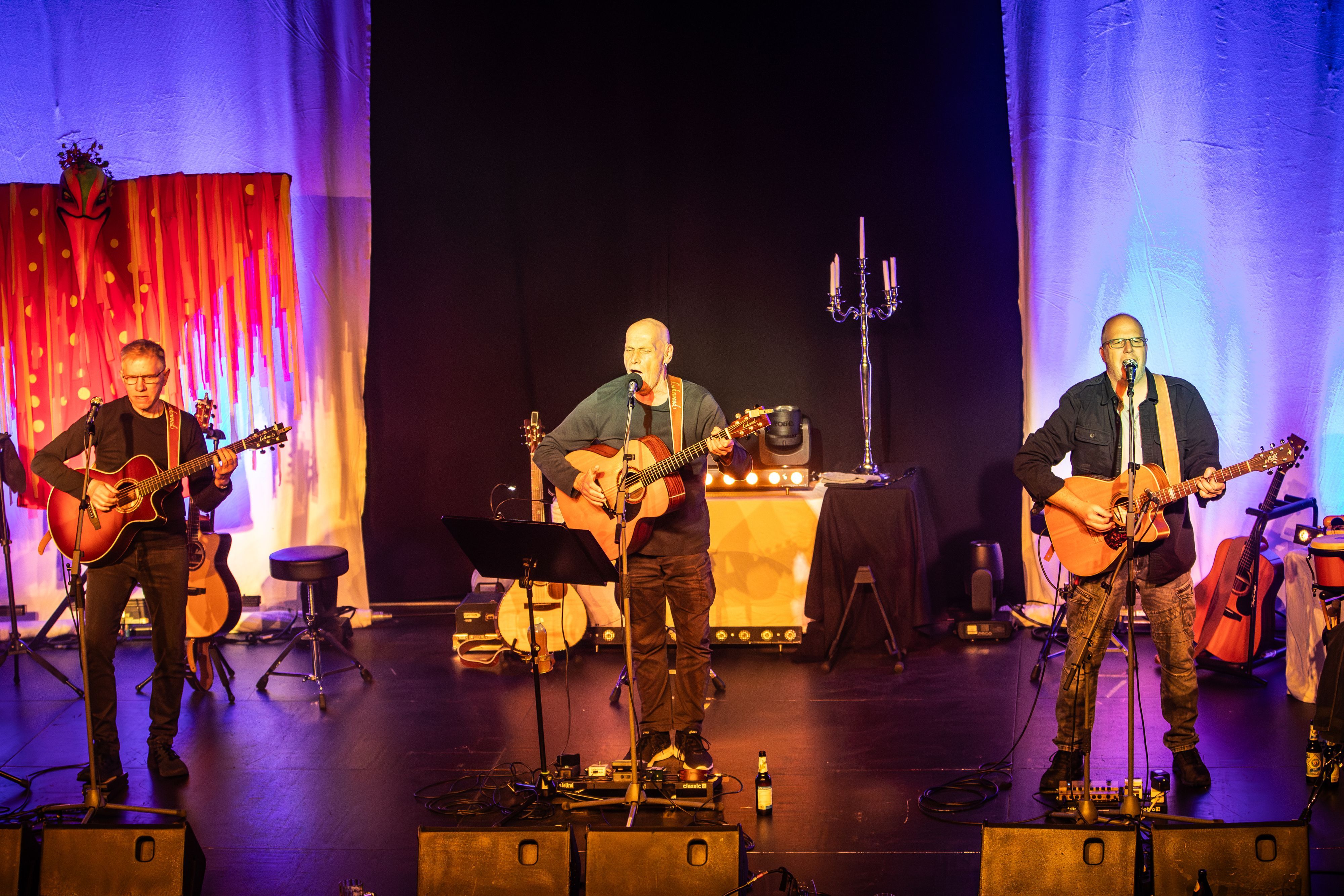 Die drei Bandmitglieder stehen auf der Bühne und performen.