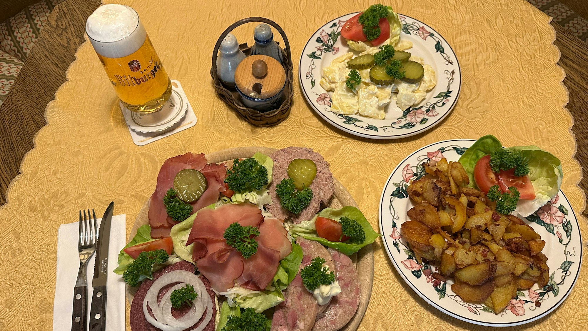Vorne der Dorfkrug Teller für 22 Euro, rechts eine Portion Bratkartoffeln, hinten der selbstgemachte Kartoffelsalat, dazu ein Bitburger Pils für 0,2 Liter für 2,20 Euro.
