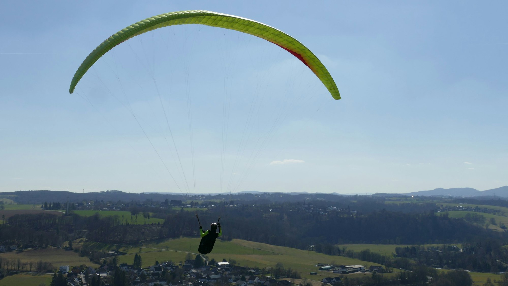 Eine Person fliegt mit einem Gleitschirm über das Siegtal.