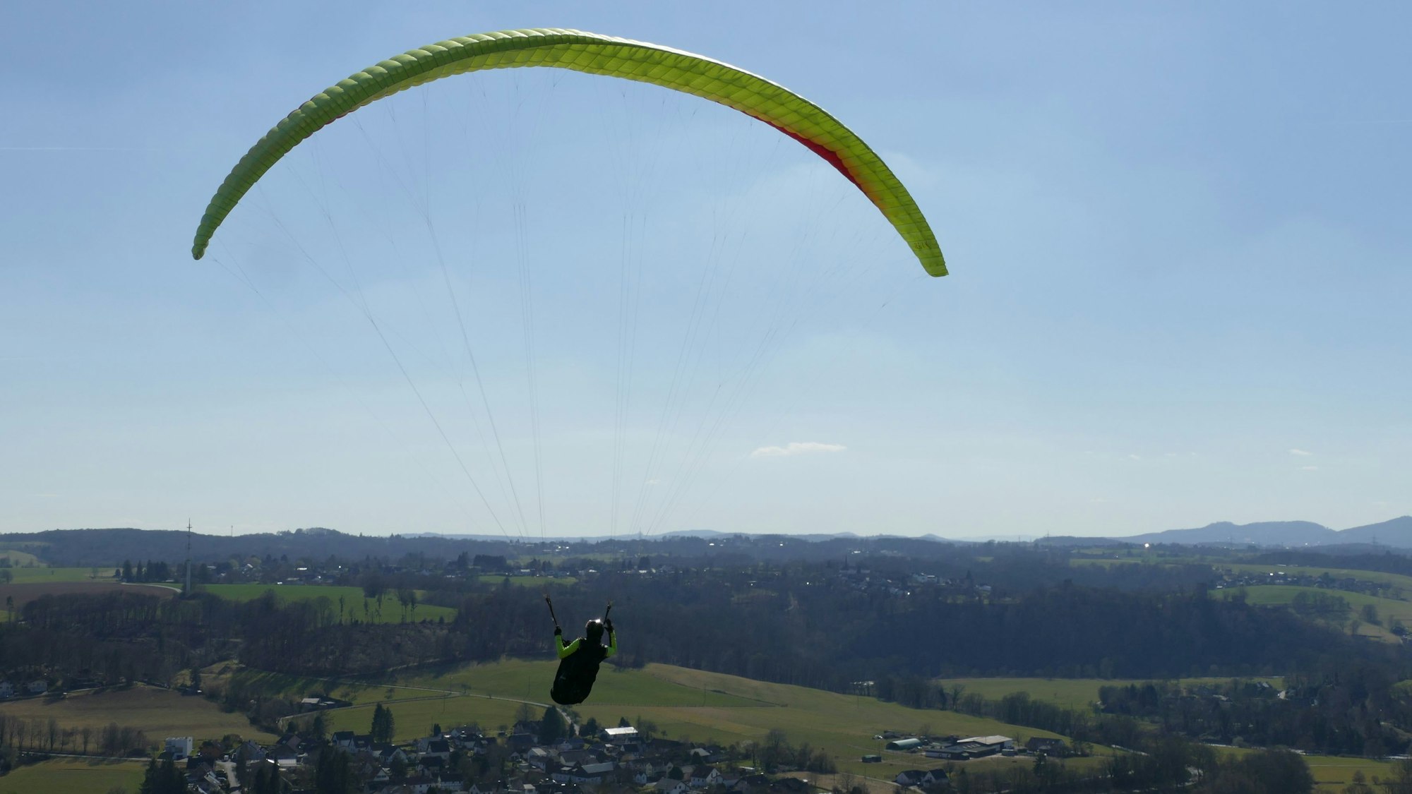 Eine Person fliegt mit einem Gleitschirm über das Siegtal.