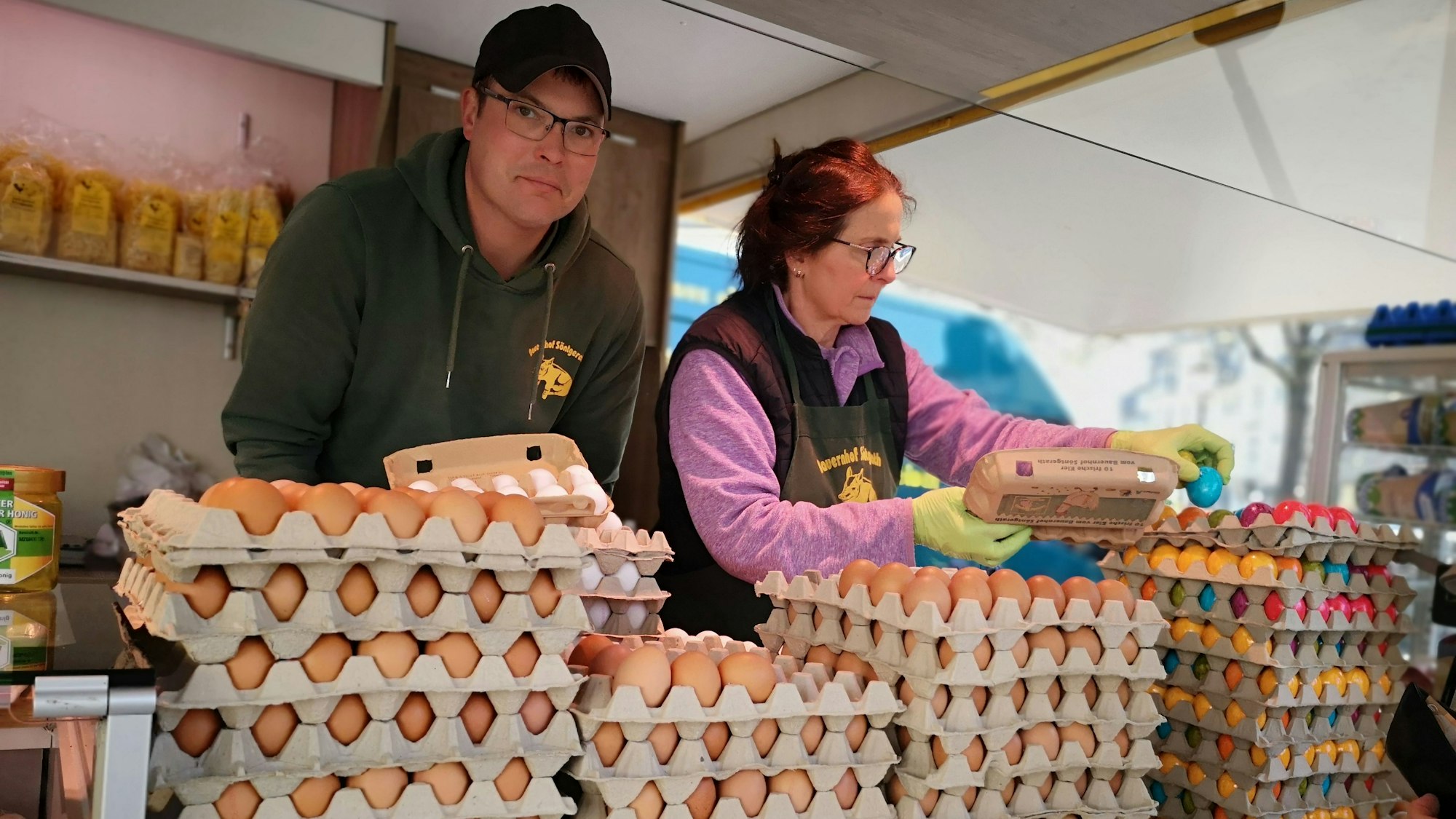 Ricardo Söntgerath und eine Mitarbeiterin stehen in ihrem Verkaufsstand auf dem Siegburger Markt vor den Eierkartons.