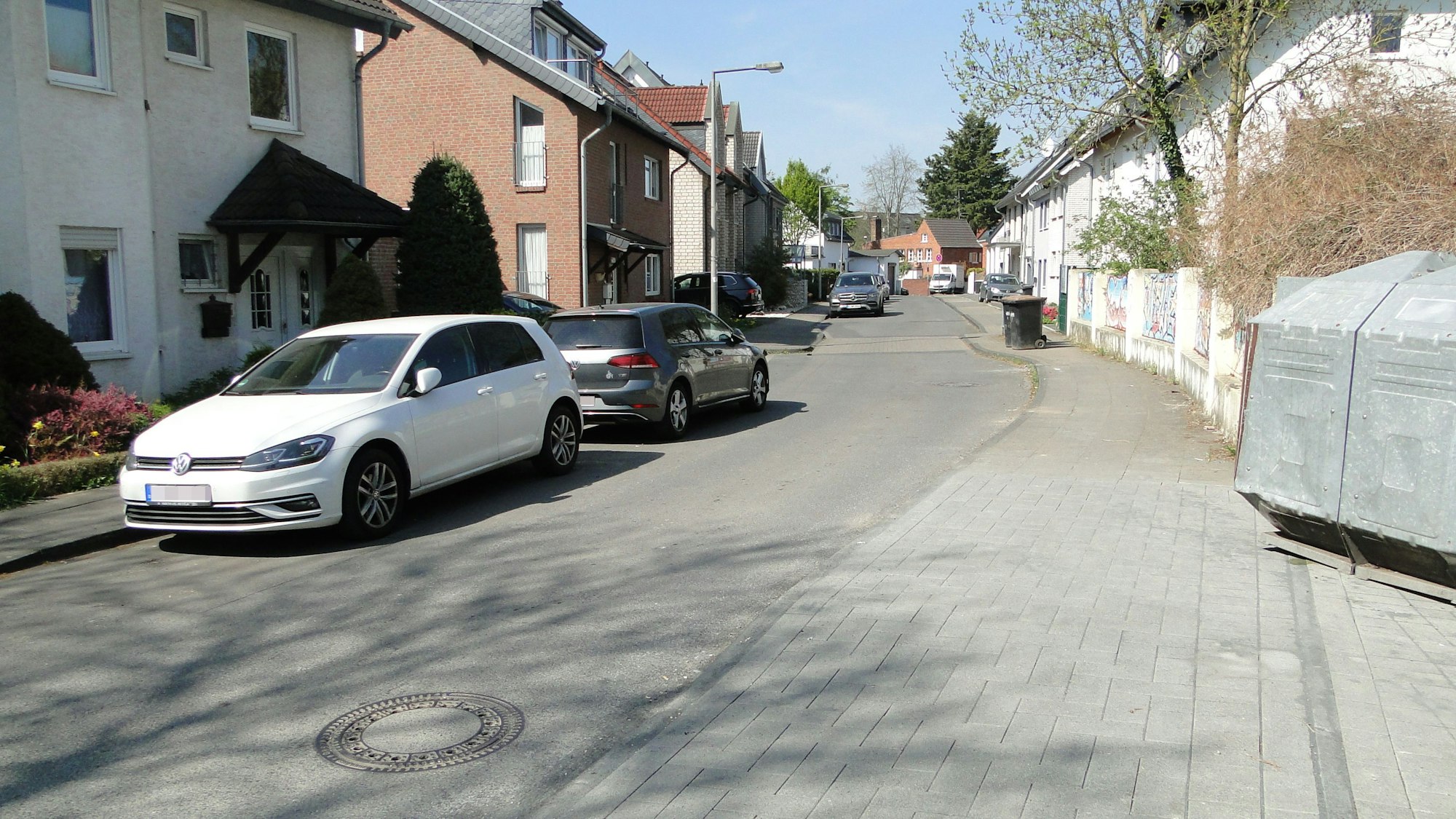 Auf einer schmalen Fahrbahn in einem Wohngebiet parken Autos am Straßenrand