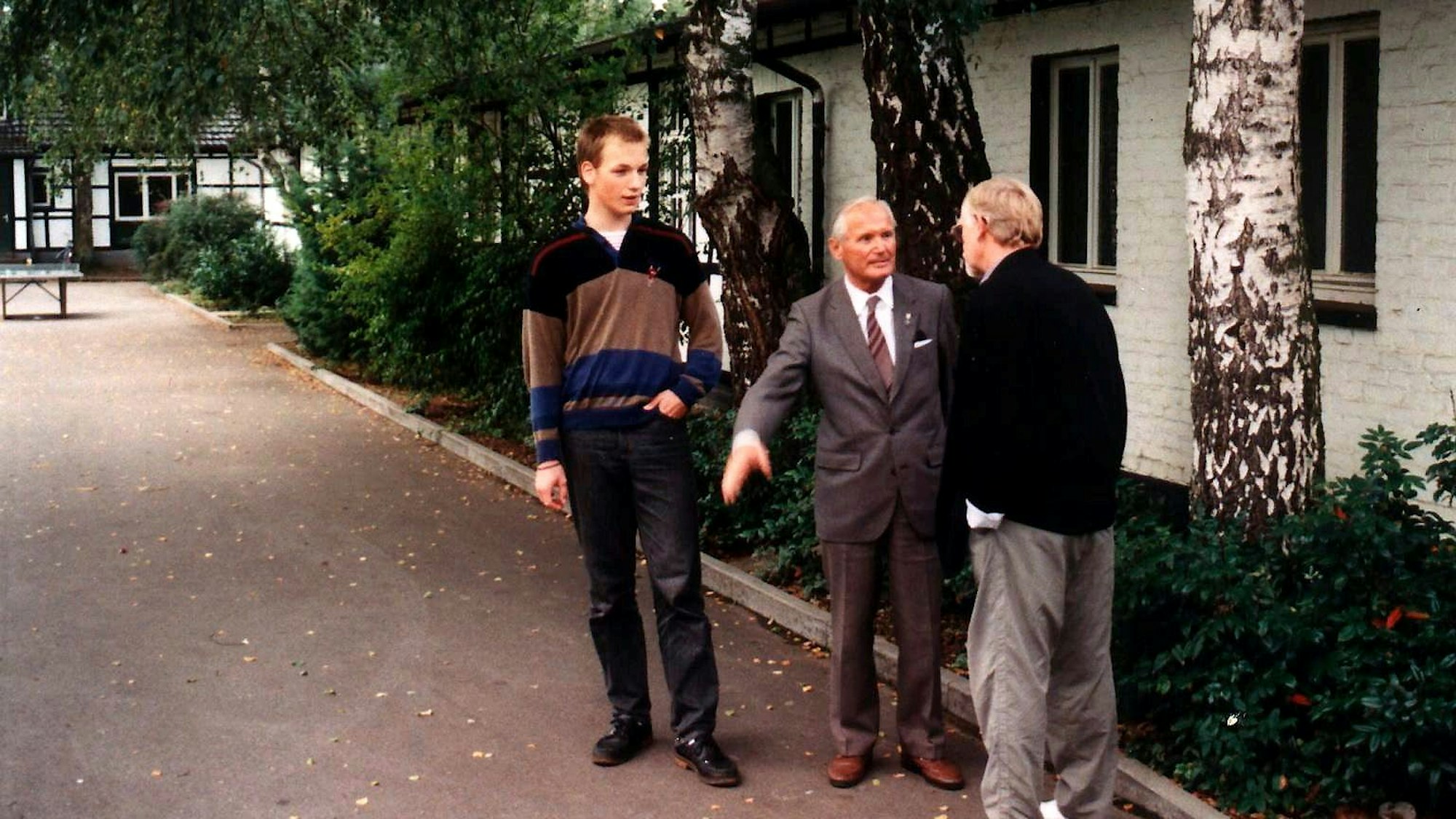 Drei Männer stehen vor historischen Gebäuden des Kinder- und Jugenddorfs Stephansheide bei Rösrath.