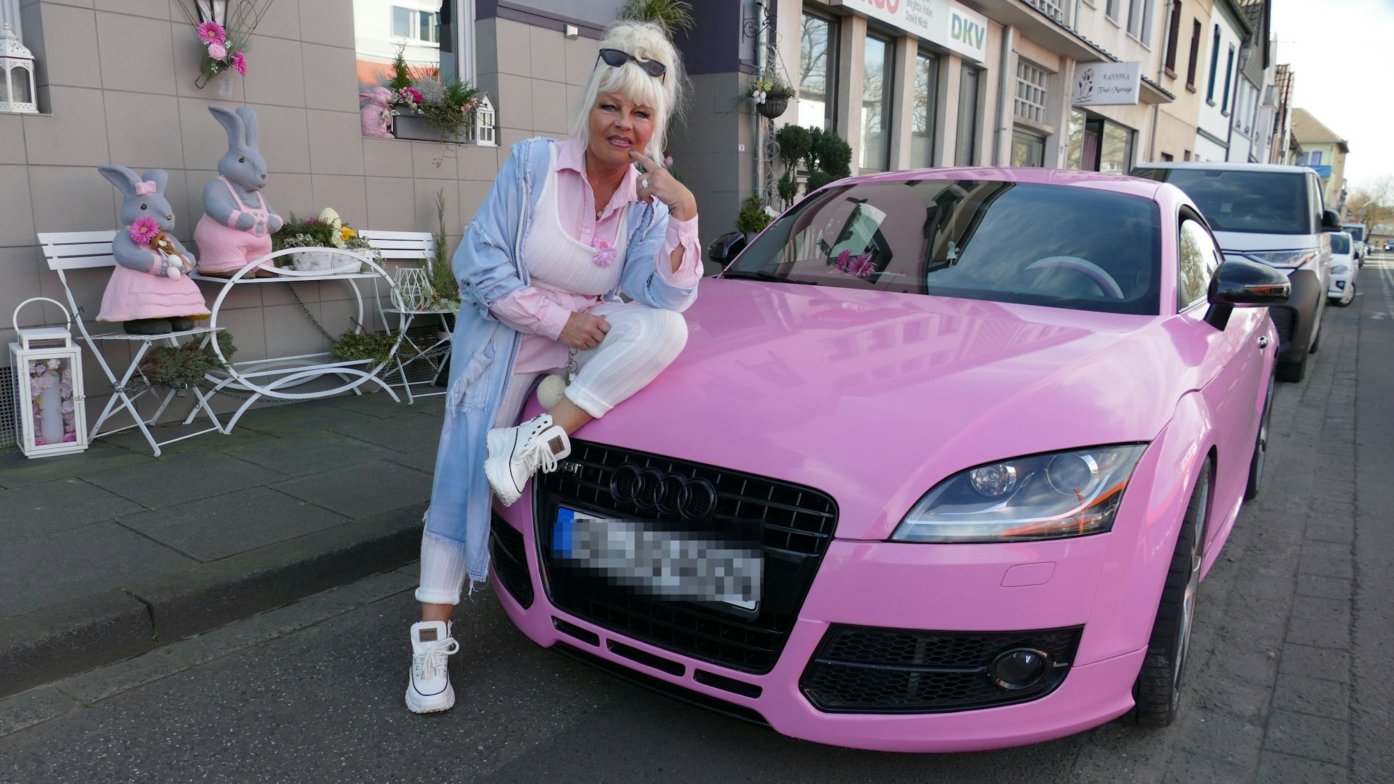 Heike Kleindienst, gekleidet in rosa und weiß, sitzt halb auf ihrem rosa Audi und lächelt. Hinter ihr sind rosa Häschendekorationen auf weißen Stühlen vor ihrem Haus platziert.