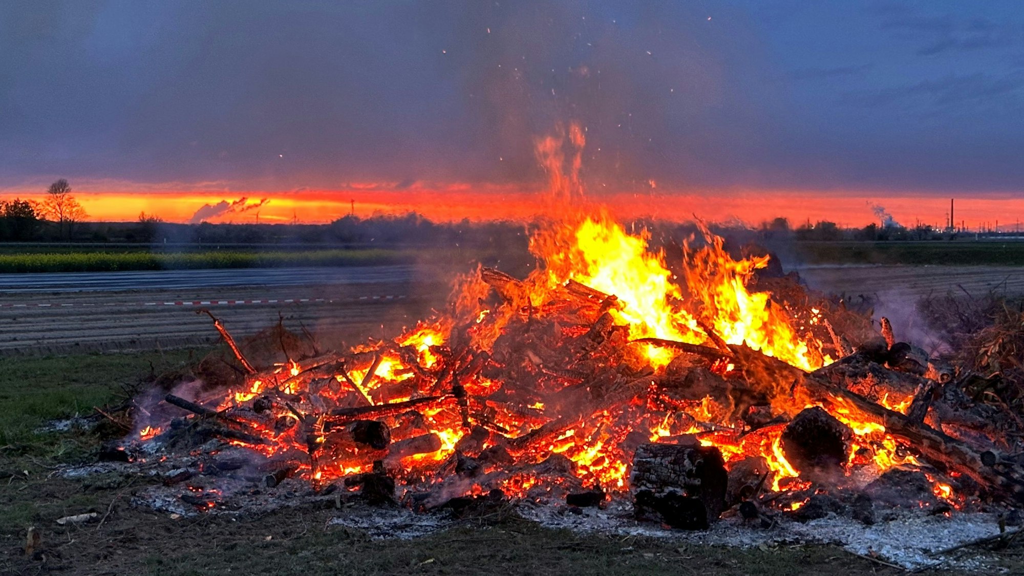 Ein großer Scheiterhaufen brennt auf einem Feld.