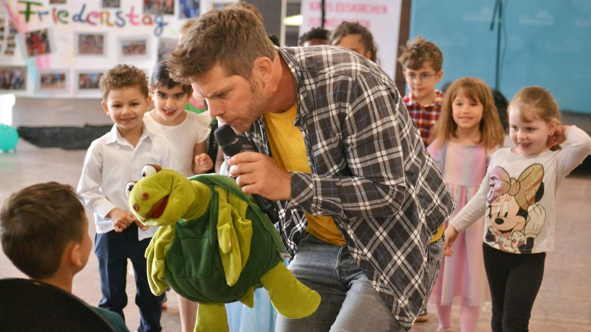 Das Bild zeigt den Sänger Uwe Reetz, der mit einer Handpuppe eine Gruppe Kinder zum Tanzen animiert.