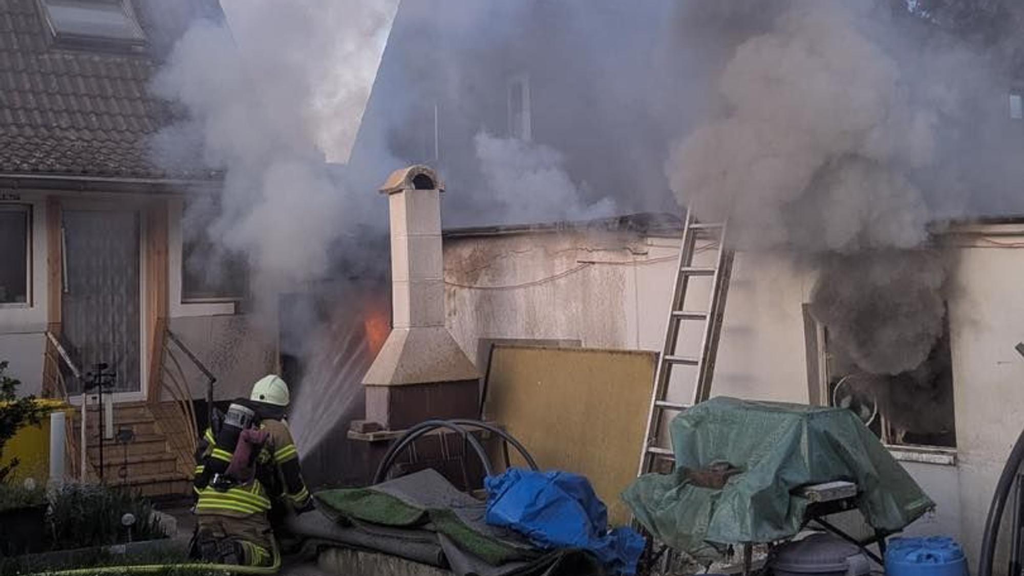 Ein Feuerwehrmann hält einen Schlauch in ein Fenster, aus dem Flammen rausschlagen.