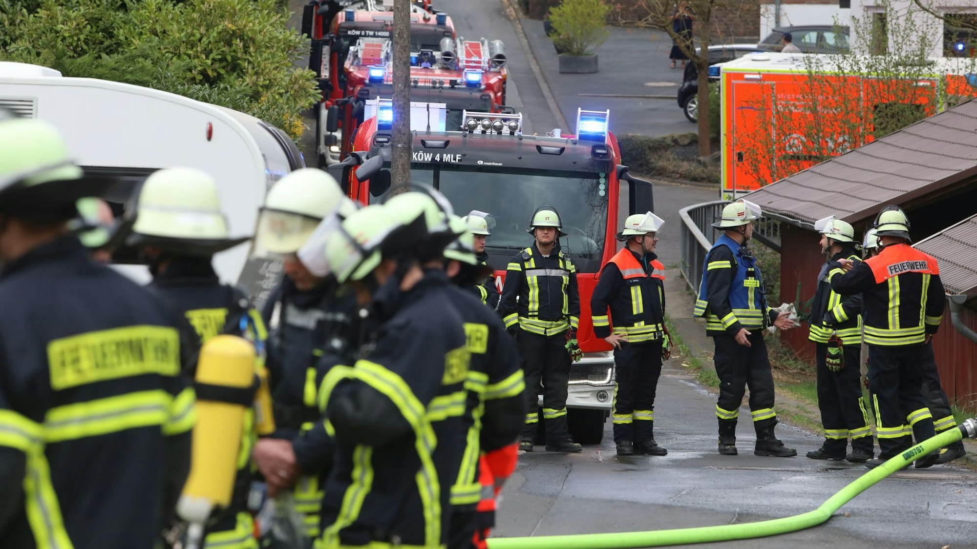 Feuerwehrkräfte stehen vor einem Haus in Oberpleis. Drei Einsatzwagen stehen mit Blaulicht an der Straße.