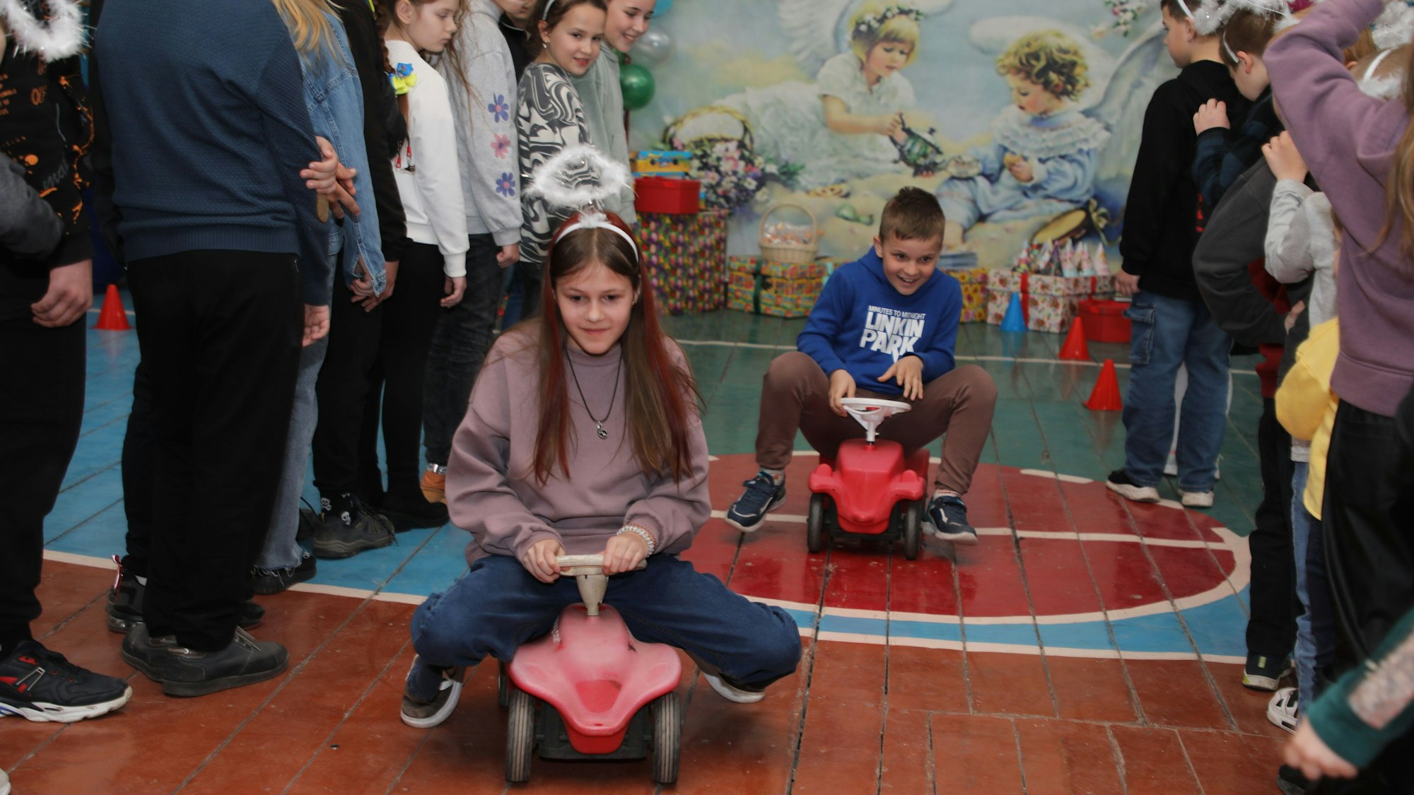Kinder fahren auf Bobbycars durch eine ukrainische Turnhalle.