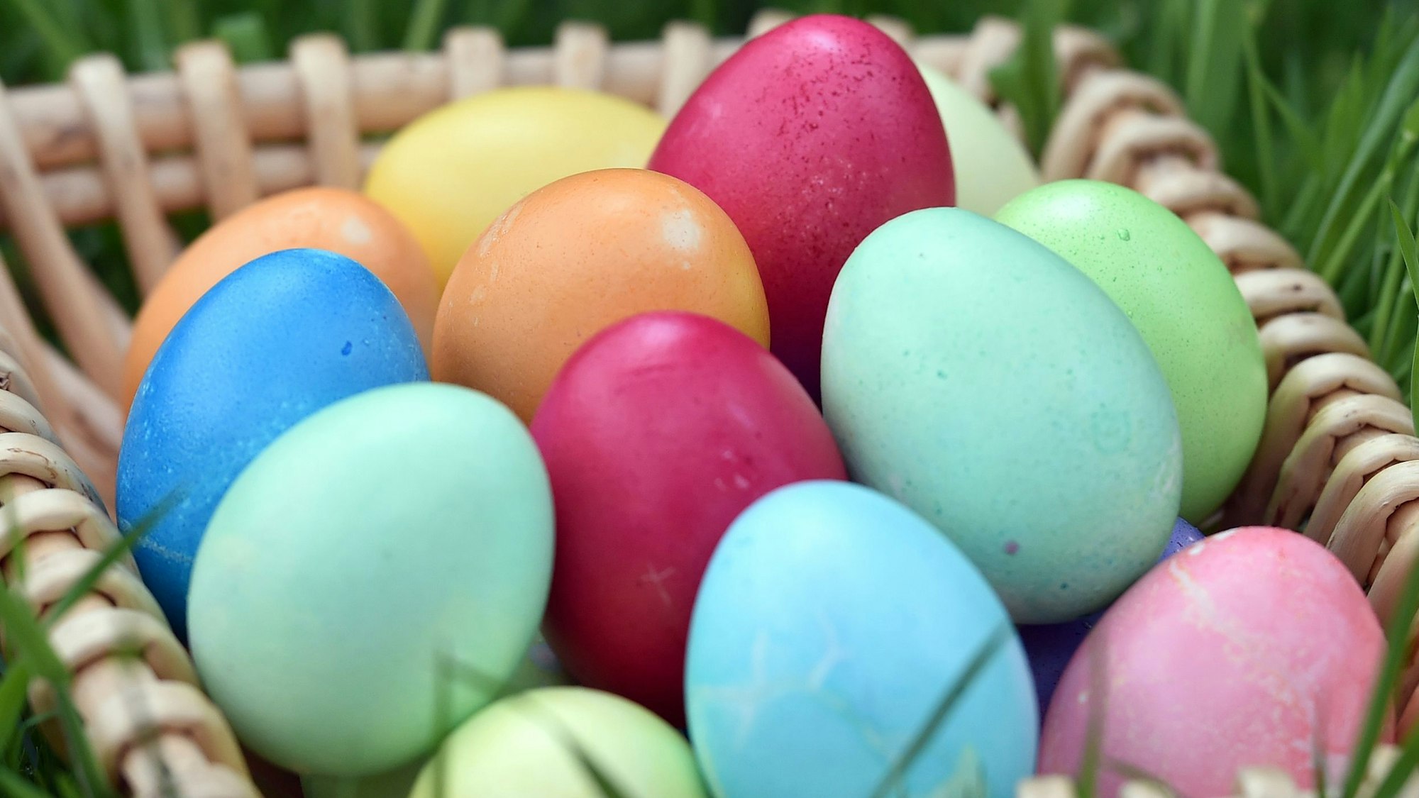 Selbstgefärbte Ostereier liegen in einem Körbchen auf einer Wiese.