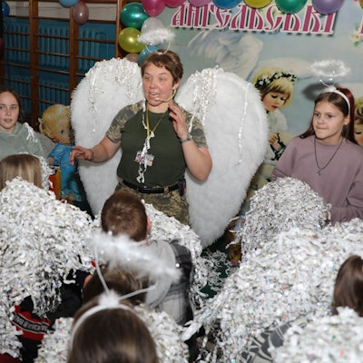 Eine Ordensschwester steht mit Engelsflügeln und Heiligenschein inmitten von ukrainischen Kindern.