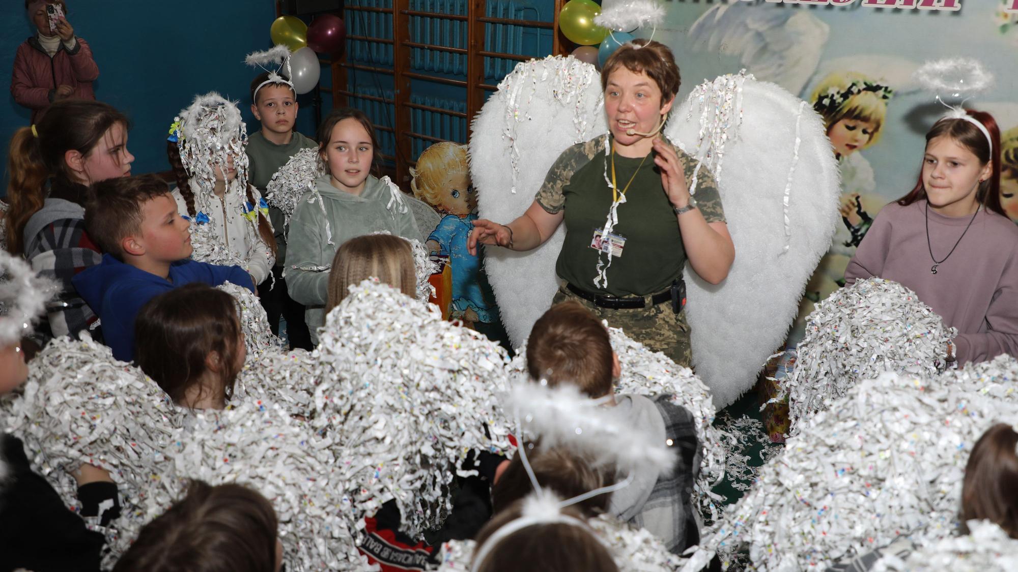 Eine Ordensschwester steht mit Engelsflügeln und Heiligenschein inmitten von ukrainischen Kindern.