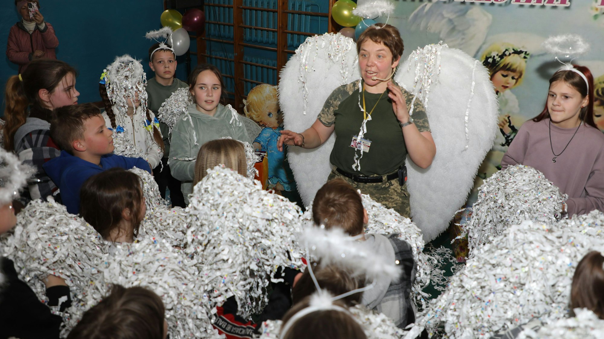 Eine Ordensschwester steht mit Engelsflügeln und Heiligenschein inmitten von ukrainischen Kindern.